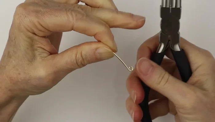 Use the larger part of the bail making pliers to form the hook shape, ensuring both hooks are the same size. File down the sharp ends.