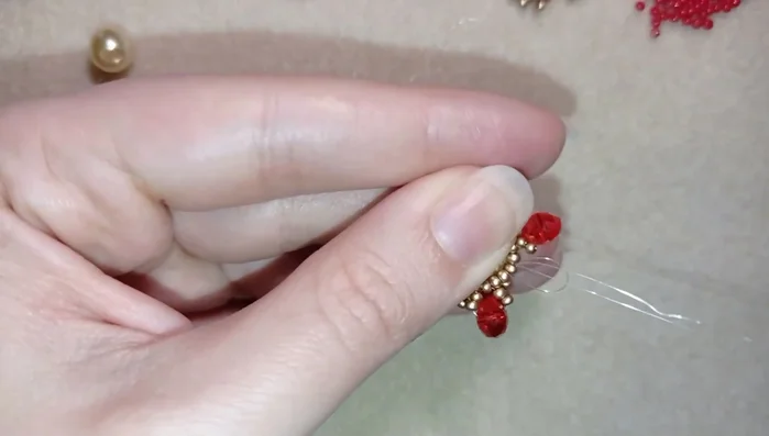 Finish the petal row, ensuring all beads are tight. Add one red bead, then another golden bead, and three more gold beads around a golden bead of the row.