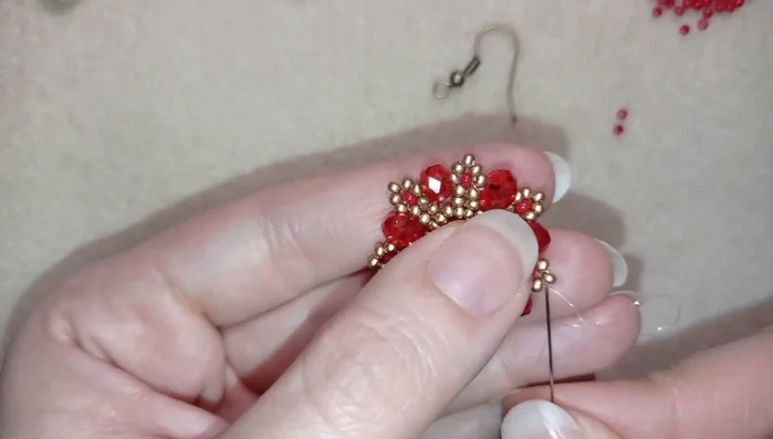 Attach the ear wire by threading a red seed bead, ear wire, and another red seed bead onto the needle. Pass the needle through a golden bead on the last row of beads, then secure with a knot and cut the thread.