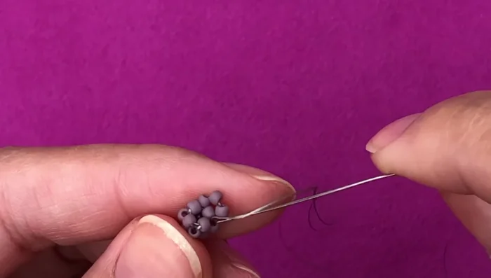 Continue building cubes: Repeat the process of adding beads and weaving them to build successive cubes atop the first. The video provides detailed step-by-step instructions (picking up 2 or 3 beads, passing through specific beads, etc.) for creating each cube face, building layer by layer.