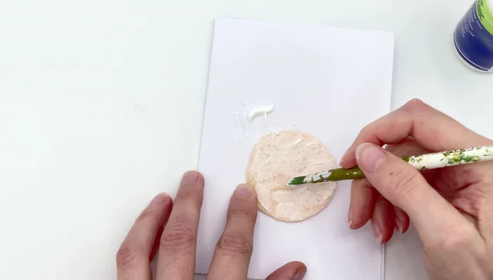 Apply fabric glue to one side of the felt circle and press it onto the back of your design, tucking in loose threads.