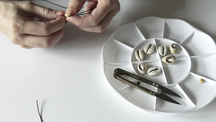 Attach a wooden bead to each end: Thread both longer cords through a wooden bead and tie a tight knot. Burn the knot ends to secure.