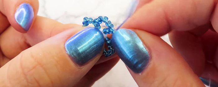 Thread the cord through the first blue bead closest to the flower, then through the previous flower's beads.