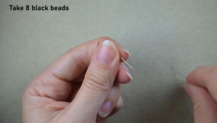 Pick up eight black beads and create a knob by looping the thread twice through the beads.