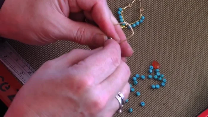 Add beads: Starting with the beading wire attached to the frame, add beads using a pattern of two and a half wraps between beads (one full wrap, another full wrap, then a half wrap before adding the next bead).