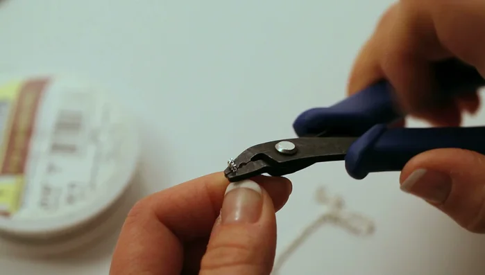 Turn the crimp tube 90° and fold it in half. Trim the wire and repeat on the other side.