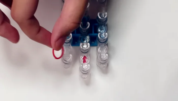 Add pink bands: Place a pink band on the first pin of the left row, stretching it to the second pin of the middle row. Repeat to the right row.