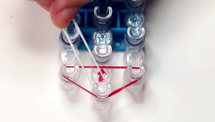 Add pink bands: Place a pink band on the first pin of the left row, stretching it to the second pin of the middle row. Repeat to the right row.