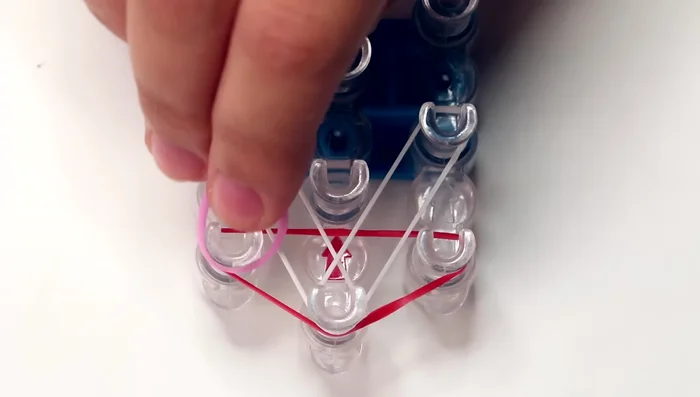 Add pink bands: Place a pink band on the first pin of the left row, stretching it to the second pin of the middle row. Repeat to the right row.