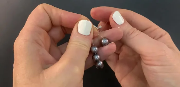 Gently pull the toothpick to tighten the knot, ensuring it tightens onto both the bracelet and itself.