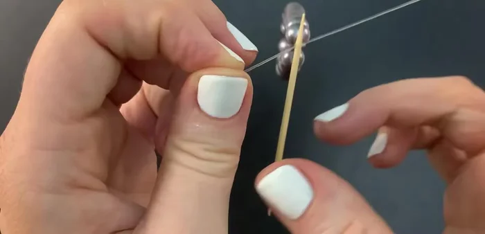 Gently pull the toothpick to tighten the knot, ensuring it tightens onto both the bracelet and itself.