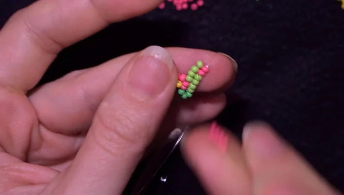 Create another flower using four pink beads, reinforcing the joint and adding a yellow bead in the center as before. Continue beading, following the herringbone stitch pattern, for a total of six rows.
