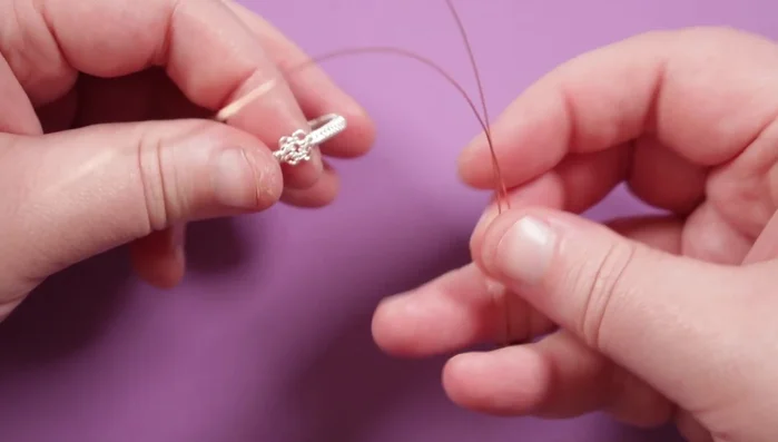 Attach the top piece to the ring band by weaving the remaining copper wire tails through the loops on the ring band. Securely wrap the wires around the loops and ring band, ensuring everything is tightly fastened.