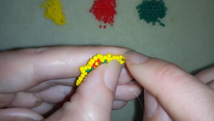 Continue adding beads in the ring band. The video demonstrates adding five yellow beads repeatedly, creating a pattern with green beads.