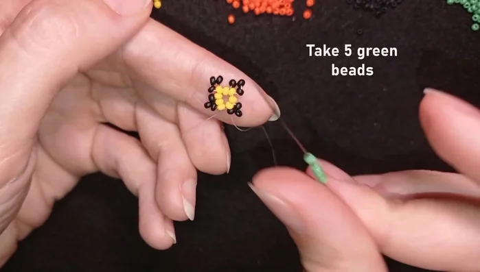 Add five green beads, skipping one bead and going through the following black bead. Repeat this pattern, adding two black beads between each set of five green beads.