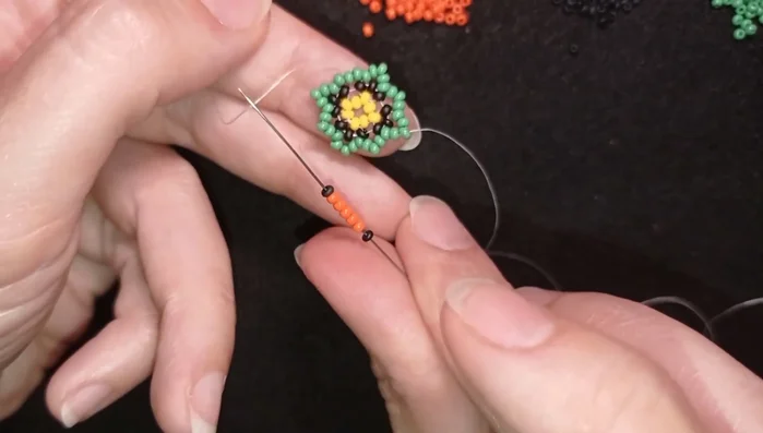 Continue adding the black, five orange beads, and black sequence, always going back through the middle bead of the previous row. Pull the thread tight and secure.