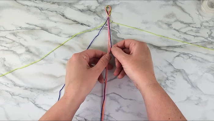 Repeat step 4, using the first strand to tie forward knots around the next color strands (orange then pink), twice for each color.