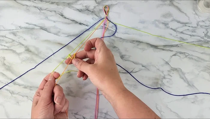 Repeat step 4, using the first strand to tie forward knots around the next color strands (orange then pink), twice for each color.