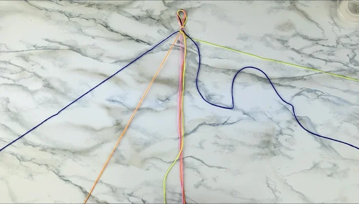 Once the first strand reaches the middle, repeat the process from the right-hand side using backward knots (mirrored number 4) instead of forward knots. Tie two backward knots for each color until both starting strands meet in the middle.