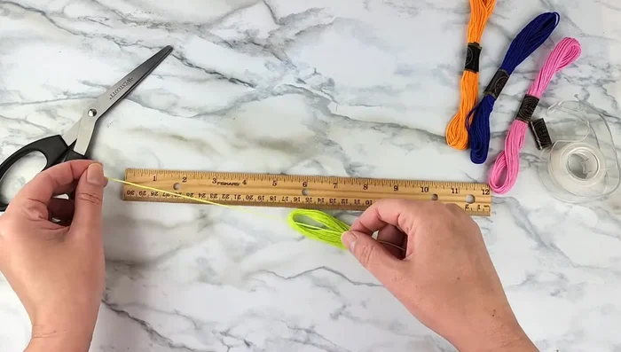 Measure and cut your string. For an 8-strand bracelet (as wide as the one in the video), use four 60-inch strands and fold them in half. Adjust the length and number of strands based on your desired bracelet width (see details in the video for different strand counts and lengths).