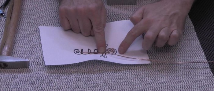 Shape the rest of the pin following the design: Use fingers and pliers to bend the wire into the desired curves and loops, securing each bend by hammering gently against the bench block to lock the shape.