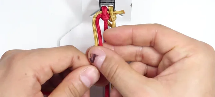 Start weaving: Create an 'S' shape with the left strands. Pass the right gold cord from the back, to the top, and through the loop on the right side. Repeat this process, creating an 'S' shape and passing the right cord through the loop on the right side with each repetition.