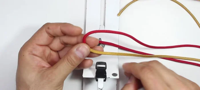 Create the bracelet core: Insert the red paracord from the top into the buckle. Pass the two gold cords through the loop on the bottom, creating a knot.