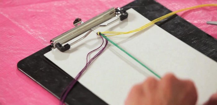 Treat each group of strands as one string. Take the first strand (e.g., purple) and bring it over the top, crisscrossing the next strand (e.g., yellow) on top of it.