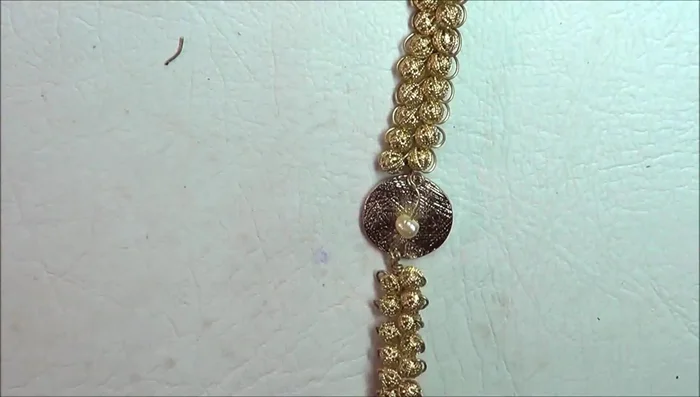 Reinforce with 28-gauge wire: Thread a length of 28-gauge wire through the holes in the disc. Secure the wire by wrapping it around the junctions of the 21-gauge wire sections to prevent the beads from pulling out. Continue wrapping the 28-gauge wire along the length of the bracelet on both sides.