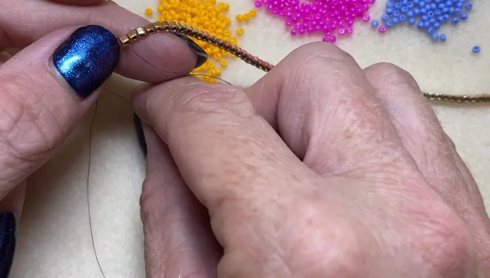 Add the triangle fringe: Coming out of a cube bead, add one size 15 seed bead, then go back into the cube bead. Move to the next cube bead and start your first color, increasing the number of size 11 seed beads (2, 3, 4, 5) in each triangle until you reach the peak. Then decrease (5, 4, 3, 2, 1) to complete the triangle. Repeat with different colored seed beads to create the bunting effect.