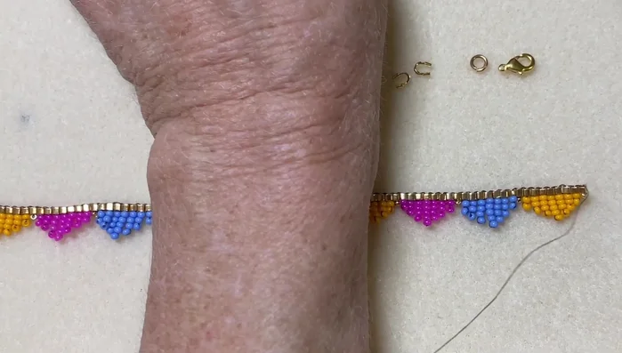 Attach the clasp: Add 1-2 seed beads to one end, attach a wire guard (optional), then add the clasp. Secure the clasp by weaving the thread through the clasp and wire guard several times.