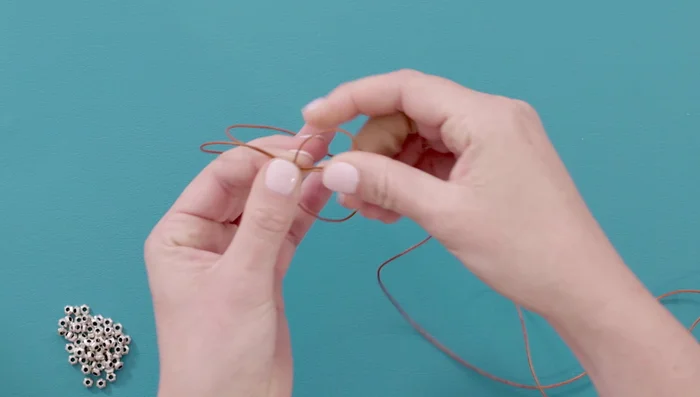 Create the initial knot: Loop the bottom leather strand over the top strand and around the back. Wrap the back strand around your finger, bring it up through the back, and then through the loop. Pull the loop closed and slide it off your finger.